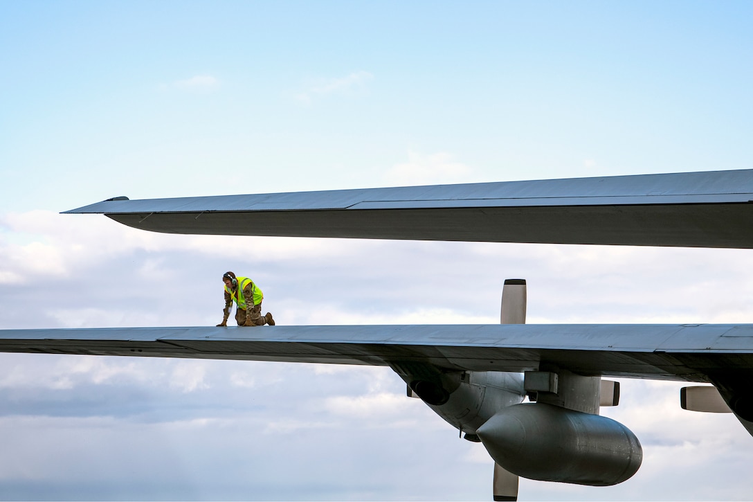 An airman kneels atop an aircraft wing.