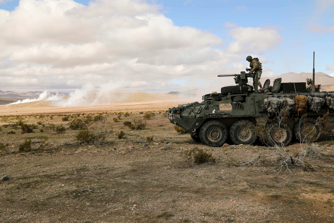 A soldier works on a machine gun atop a military vehicle.