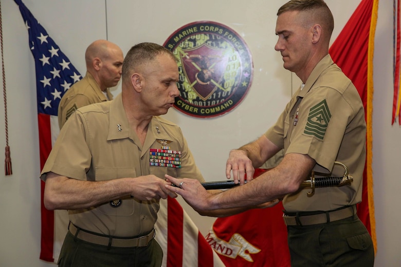 Maj. Gen. Matthew G. Glavy, Marine Corps Forces Cyberspace Command and Joint Task Force Ares commander, passes the sergeant major's sword to Sgt. Maj. Jay D. Williamson during a relief and appointment ceremony in Lasswell Hall. Sgt. Maj. Daniel L. Krause relinquished his duties as the sergeant major of MARFORCYBER while Williamson was appointed to fill the role during the ceremony held at Fort Meade, Maryland, Mar. 19, 2020. (Department of Defense photo by Joseph Wilbanks)