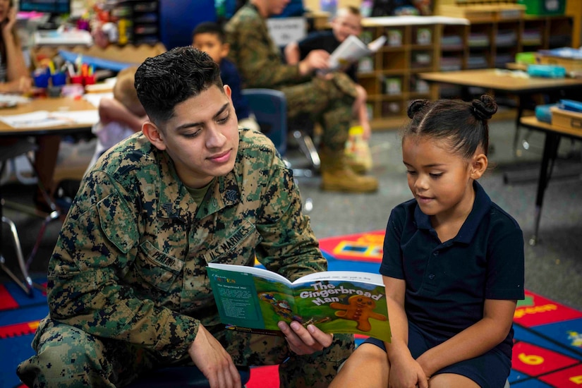 A Marine reads a book to a young child.
