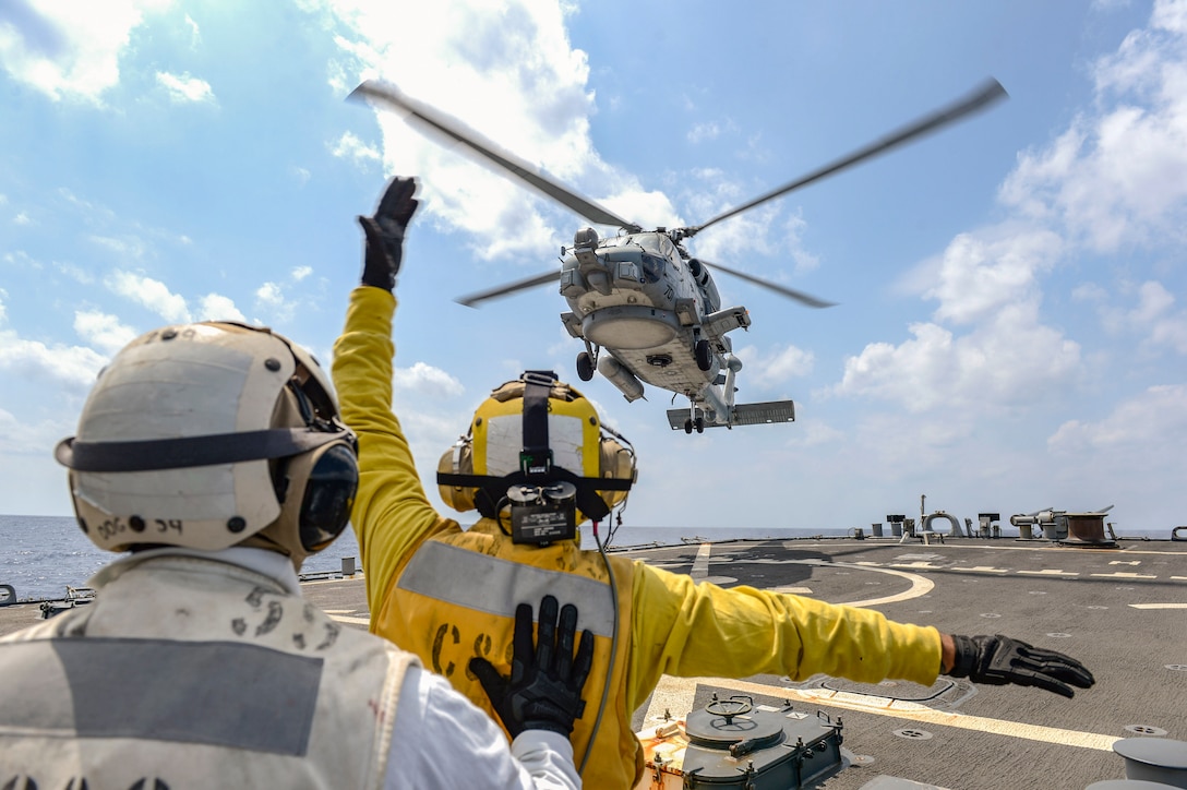 A sailor signals to a helicopter on a ship's flight deck.