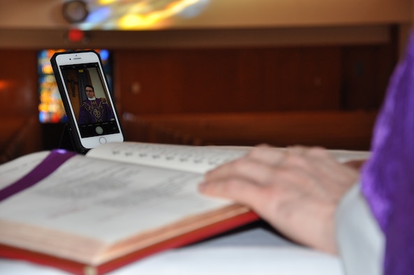 Hand of a chaplain on a bible with a smart photo recording a mass with empty pews.