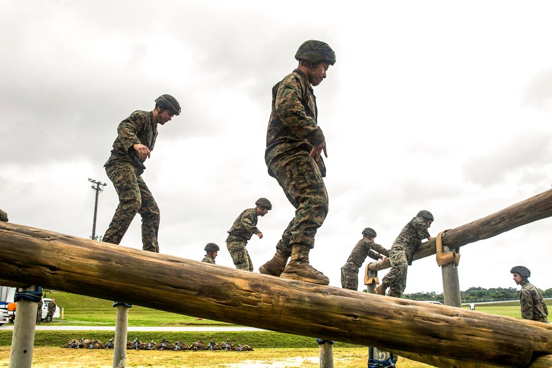 Marines walk on a wood obstacle.