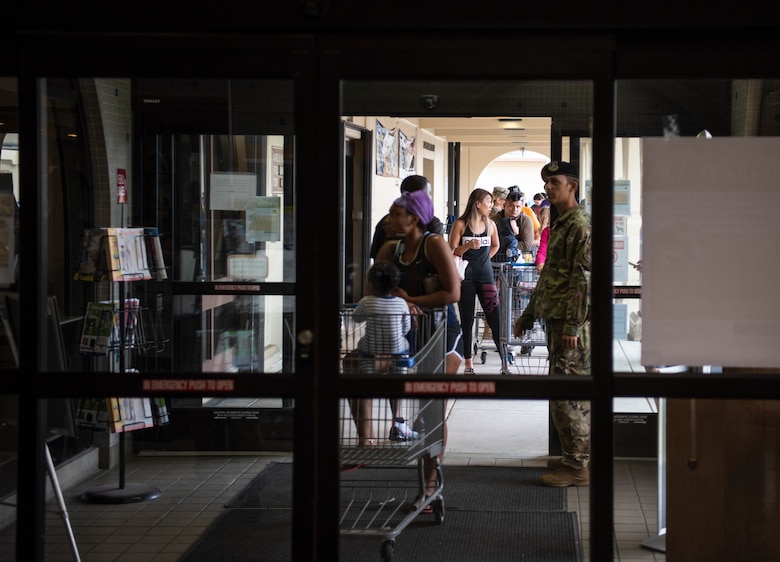 Service members and their family members wait in line to enter the commissary at Andersen AFB, Guam, March 17, 2020. In response to COVID-19, Brig. Gen. Gentry Boswell, 36th Wing commander, declared a health emergency, which includes limiting base access to mission-essential personnel, closure of public facilities and enforcing social distancing with no person-to-person contact. (U.S. Air Force photo by Airman 1st Class Michael S. Murphy)