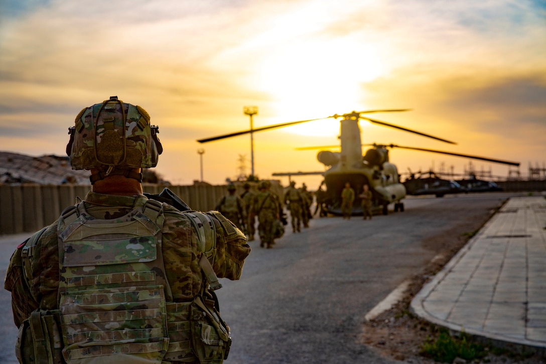 Soldiers walk in a line toward a parked and open Chinook.