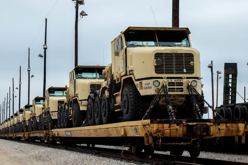 Military vehicles are loaded atop rail cars.