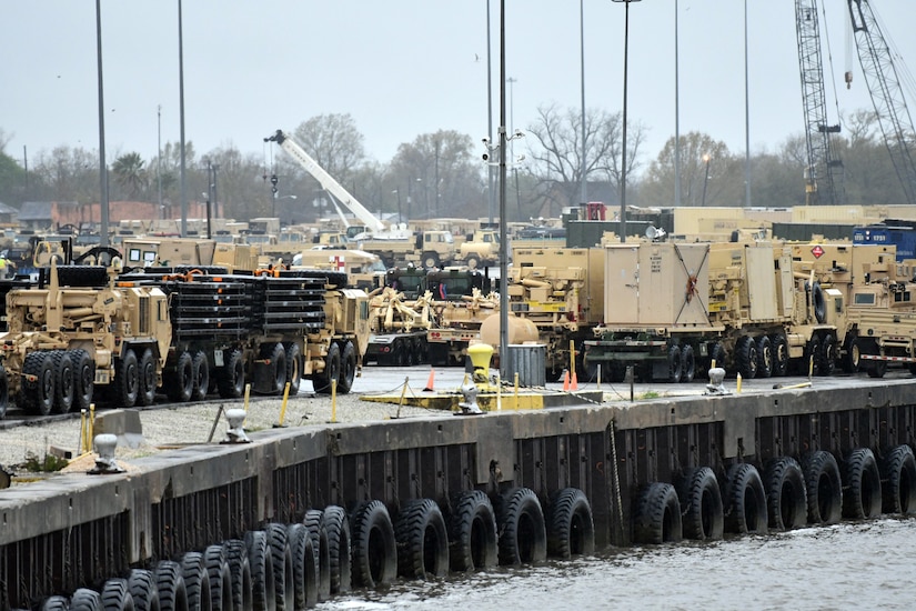 Dozens of military vehicles are marshalled at a port.