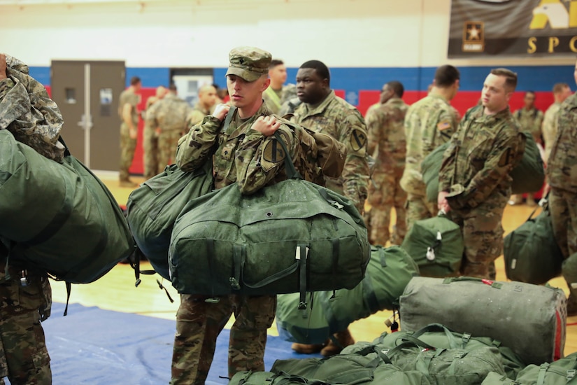 Service members carry mobility bags indoors.