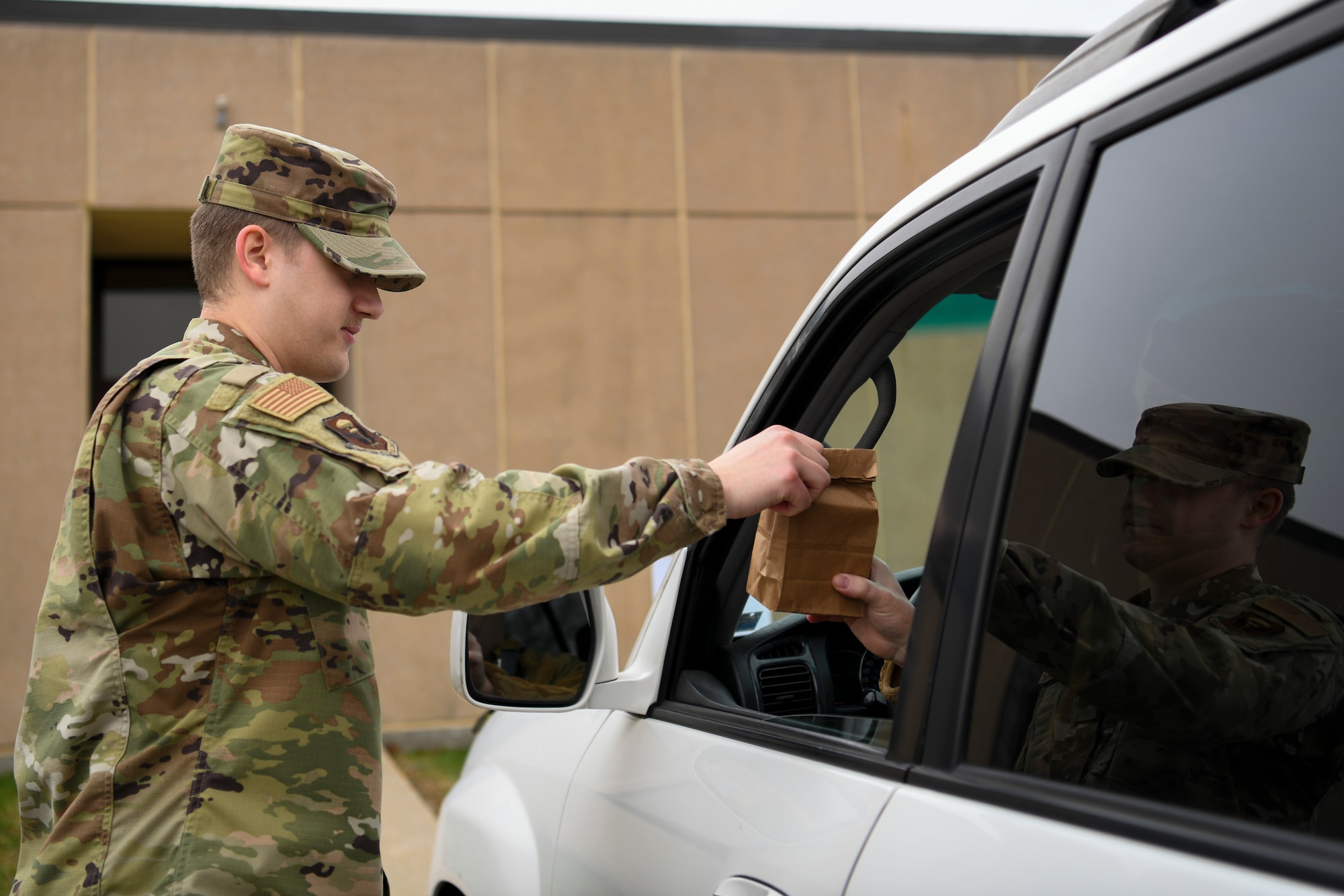 U.S. Air Force Staff Sgt. Nathan Jones, a 509th Operational Medical Readiness Squadron bioenvironmental technician and pharmacy augmentee, delivers prescriptions to a patient outside the 509th Medical Group, at Whiteman Air Force Base, Missouri, March 20, 2020. The medical group’s pharmacy implemented curbside pickup pharmacy procedures. The new service allows individuals with called-in refills and activated prescriptions to park in a designated parking spots and have their prescriptions delivered to the car. This procedure is part of the effort to limit visiting the facility. (U.S. Air Force photo by Staff Sgt. Dylan Nuckolls)