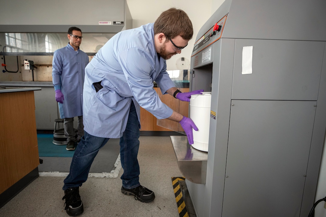 Code 134, Laboratory Division, chemist Anthony Painter places a container of isopropyl alcohol-based hand sanitizer ingredients into the Puget Sound Naval Shipyard & Intermediate Maintenance Facility accredited laboratory's mixing machine, in Building 59, March 20, 2020. (PSNS & IMF photo by Scott Hansen)
