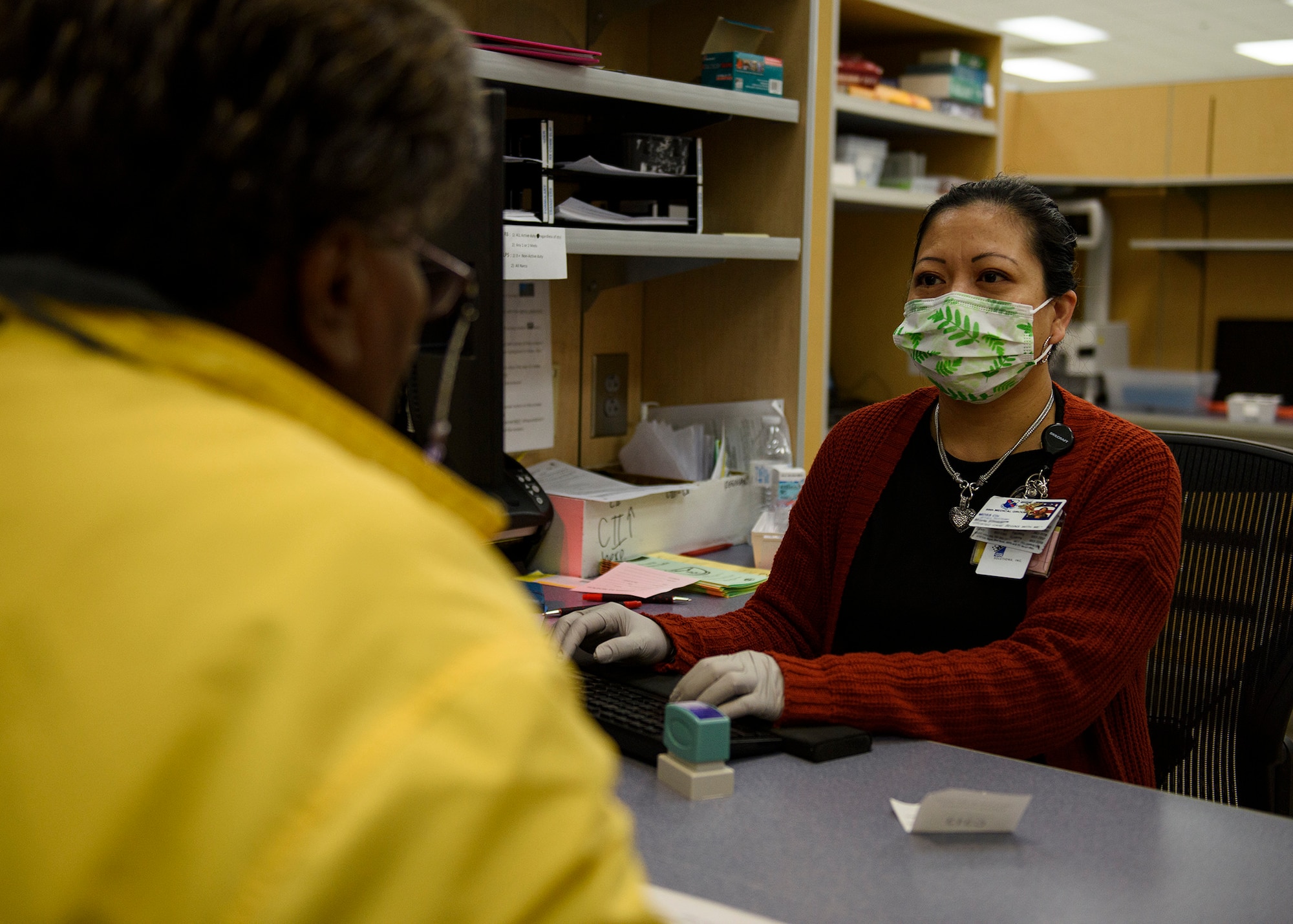 A pharmacist technician speaks for a patient at a desk.