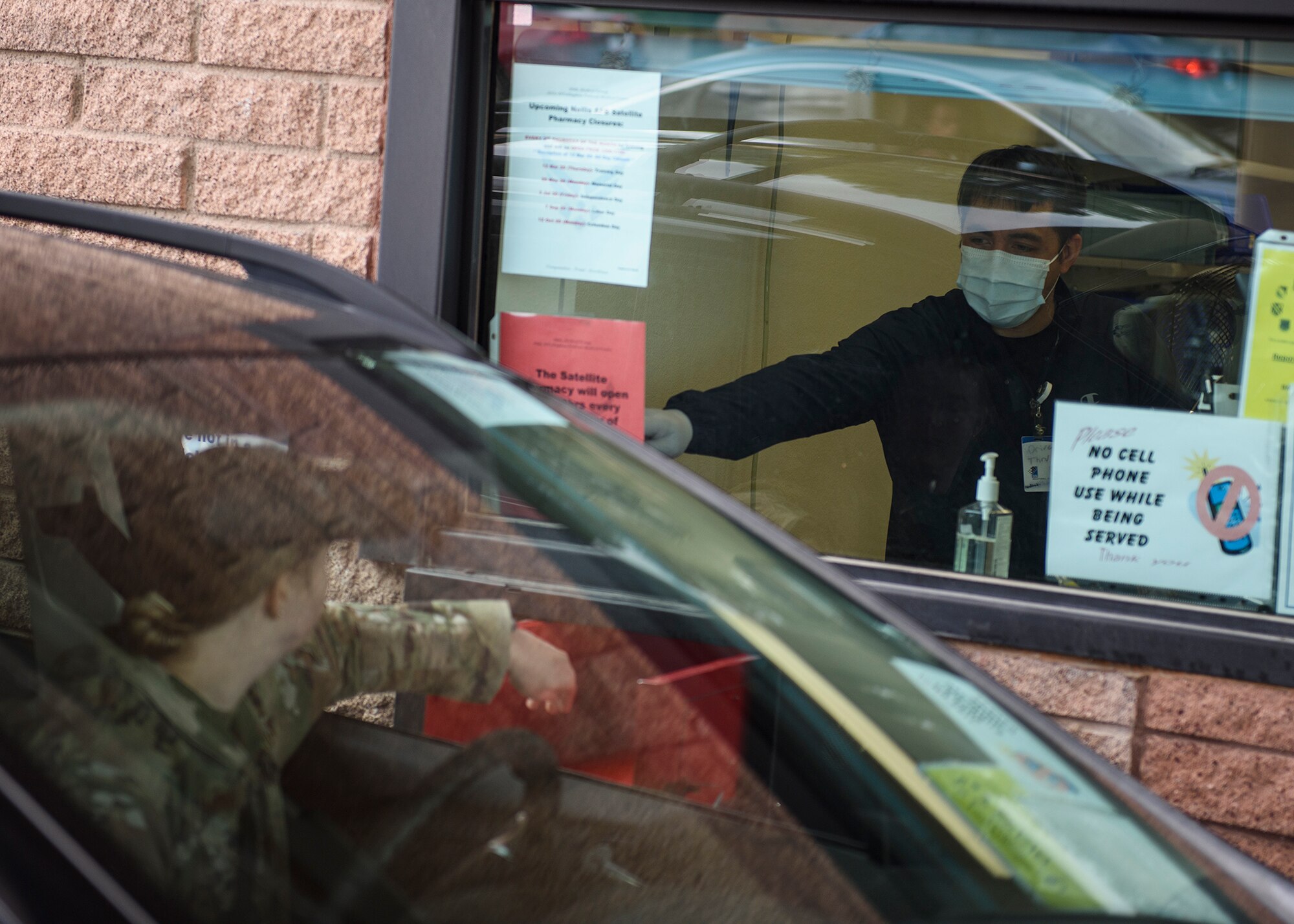 A pharmacist technician passes prescriptions to an Airman through the drive-thru.