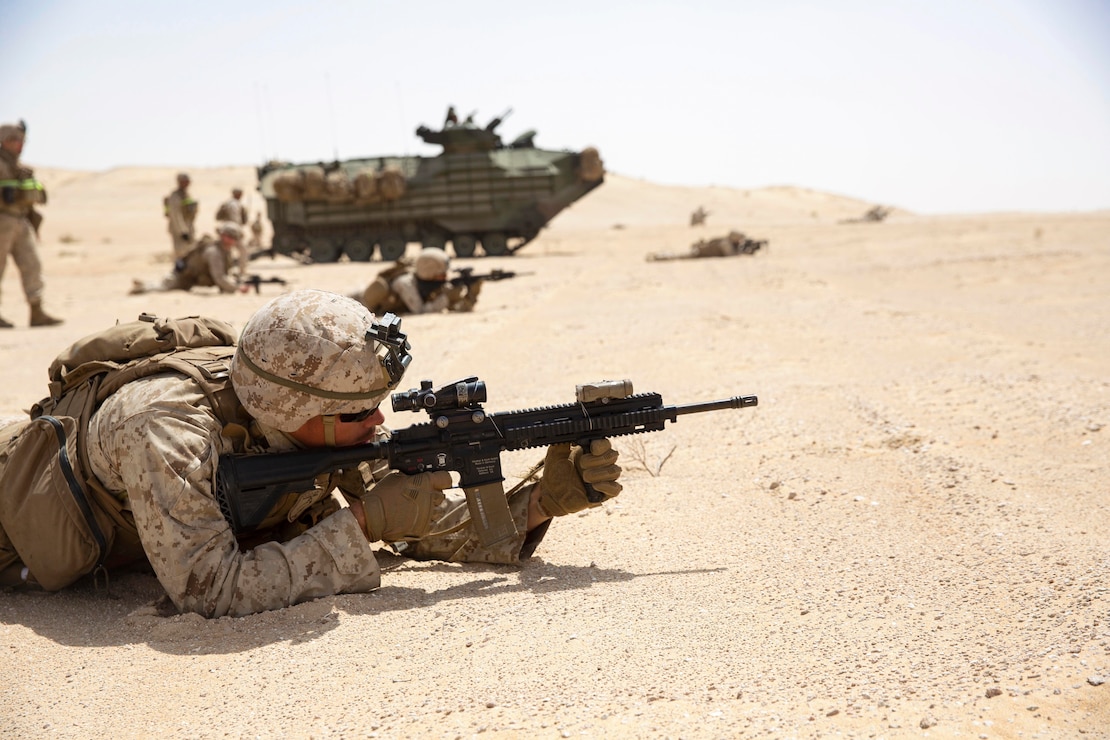 A group of Marines aim weapons in a dirt area.