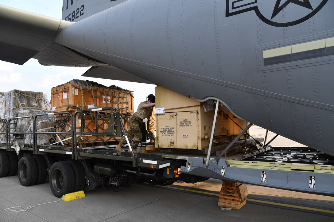 Airmen push a pallet of cargo up the loading ramp of a transport aircraft.