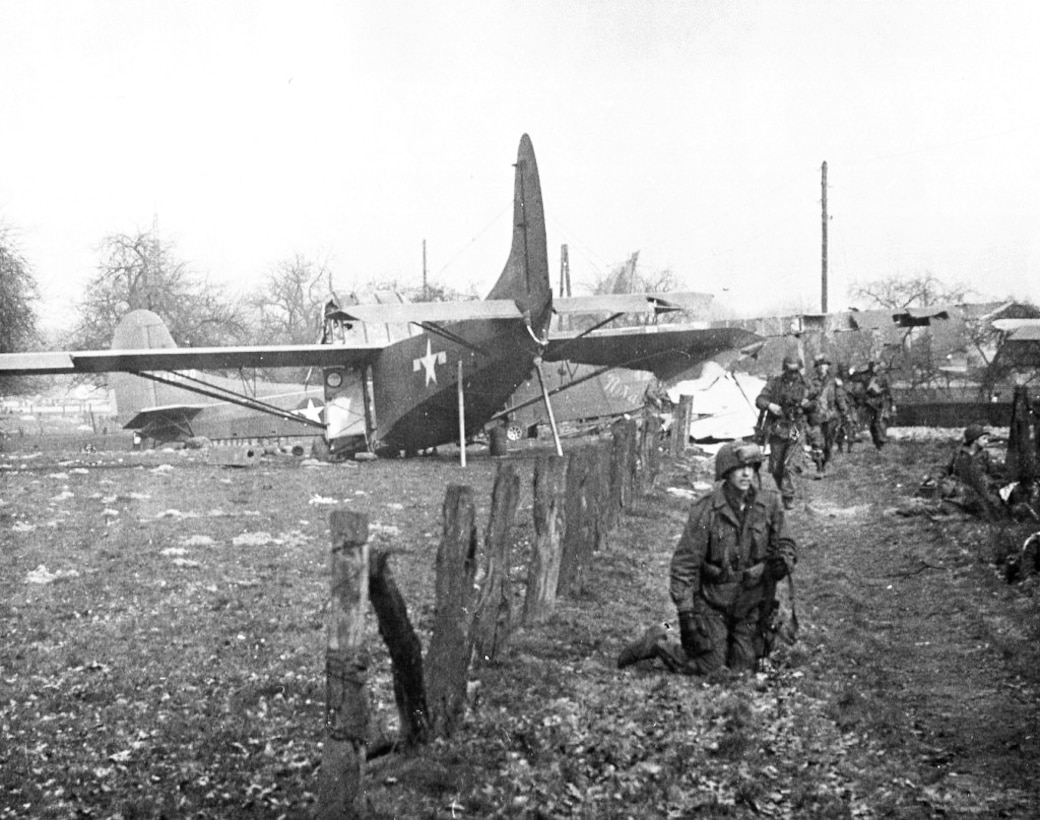 Troops move down a dirt road away from an airplane.