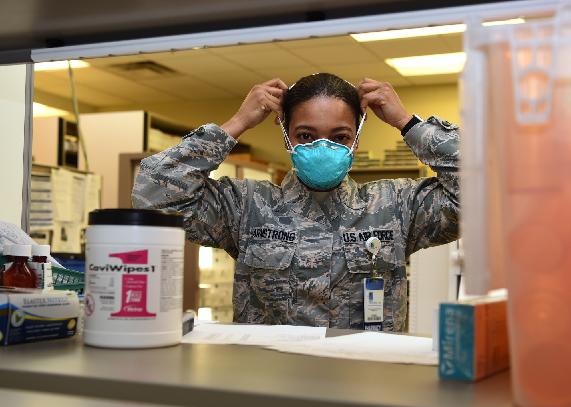 U.S. Air Force Staff Sgt. Montea Armstrong, 17th Medical Group pharmacy technician, applies proper protective gear for heightened exposure risks with customer interactions at the Ross Clinic’s pharmacy on Goodfellow Air Force Base, Texas, March 23, 2020. With Goodfellow’s Health Protection Condition in BRAVO, Armstrong wore a mask to avoid contamination of COVID-19. Goodfellow currently has no confirmed COVID-19 cases.  (U.S. Air Force Photo by Airman 1st Class Abbey Rieves)