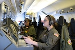 Several sailors monitor a console on an aircraft.