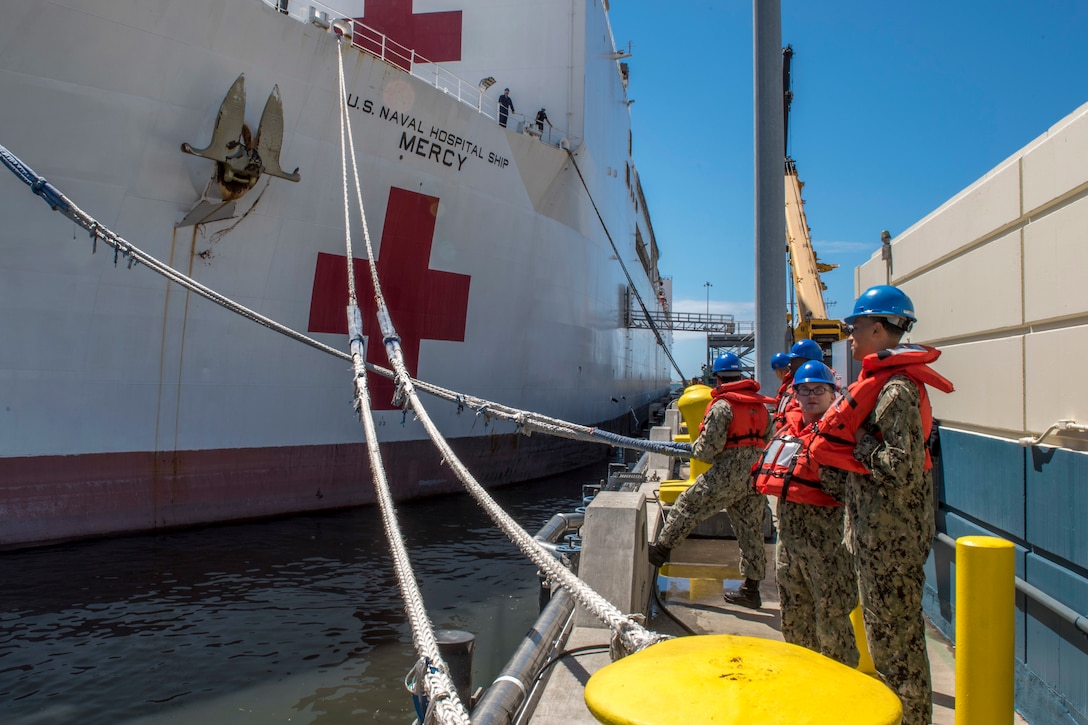 Sailors stand on a dock next to a hospital ship.