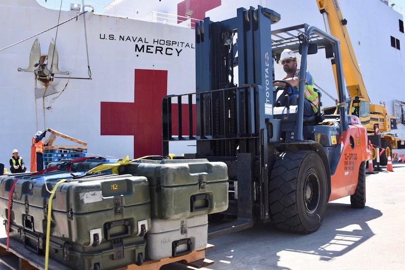 A forklift driver loads supplies from a dock onto a ship.