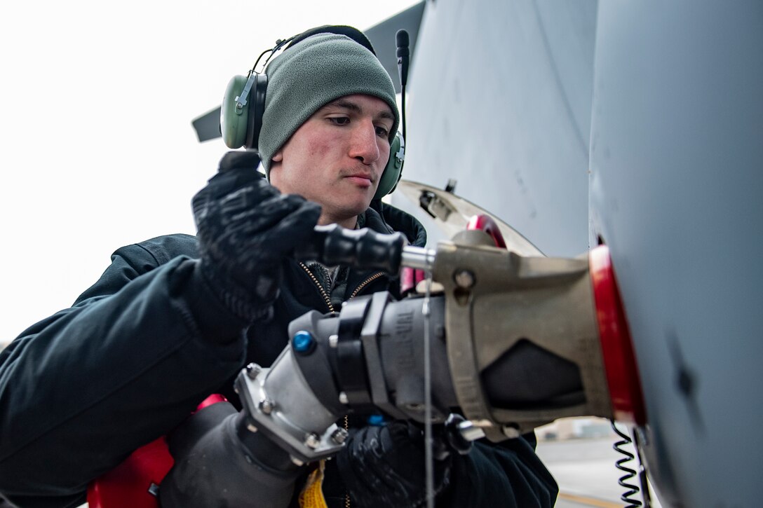 A man attaches a hose to a military aircraft.