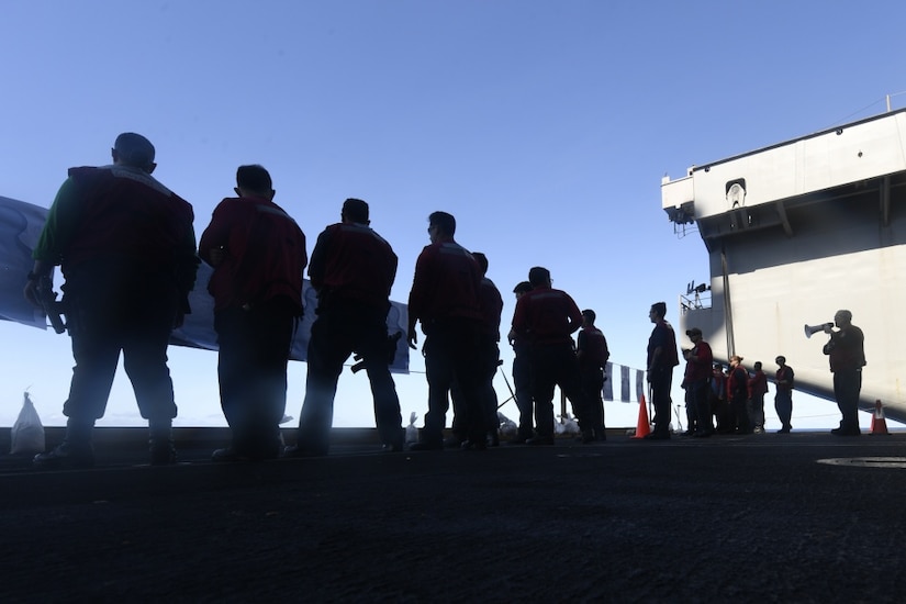 Sailors stand on aircraft carrier deck.