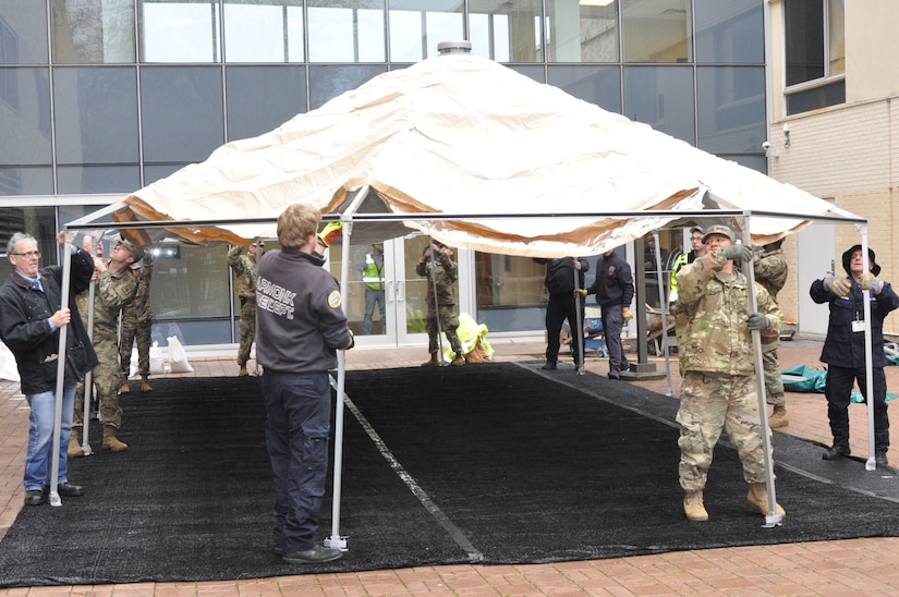 Soldiers and civilians put up a tent near an office building.