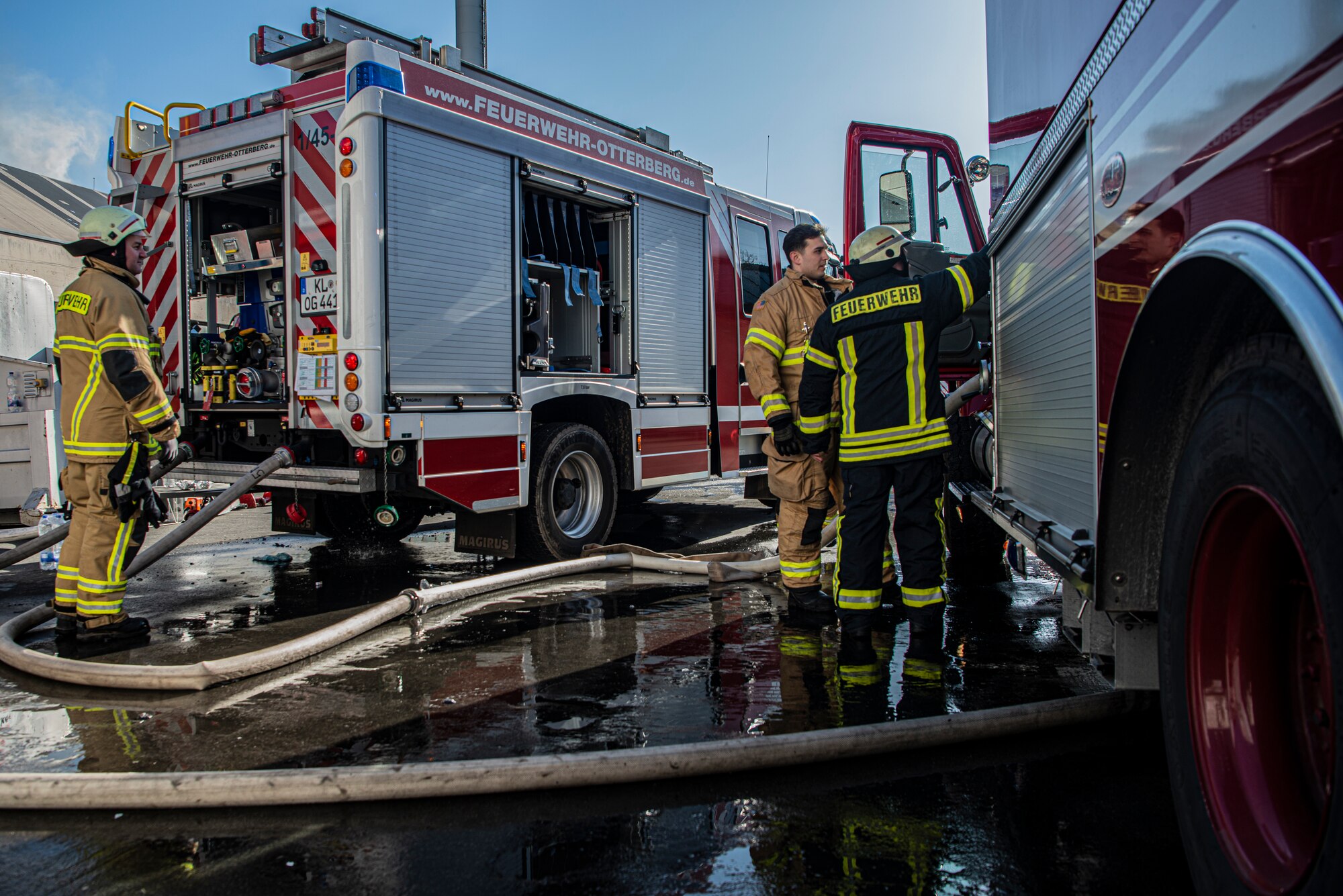 Three firefighters prepare to attach hoses from one truck to the other in Otterberg, Germany, March 23, 2020.