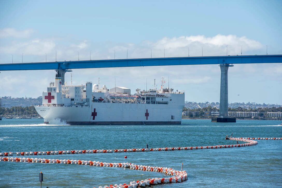 A military hospital ship sails under a bridge as it makes its way out to sea.