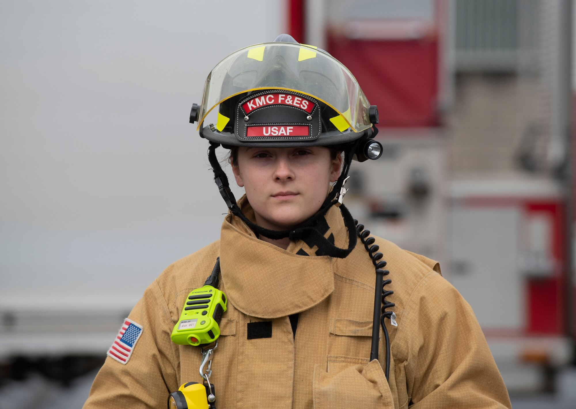 A firefighter poses in gear in front of a fire truck
