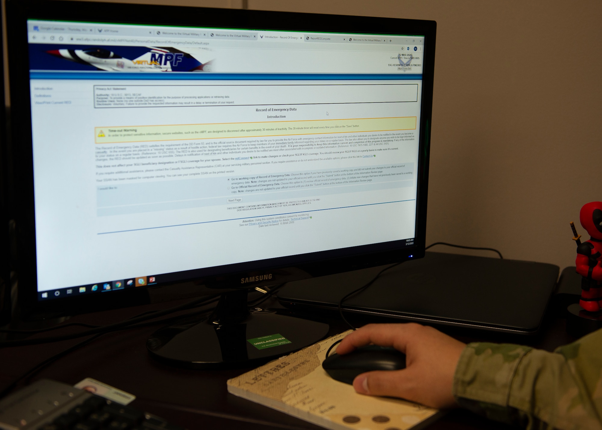 image of airman's hand on computer mouse in foreground with computer screen image on the record of emergency data introduction page