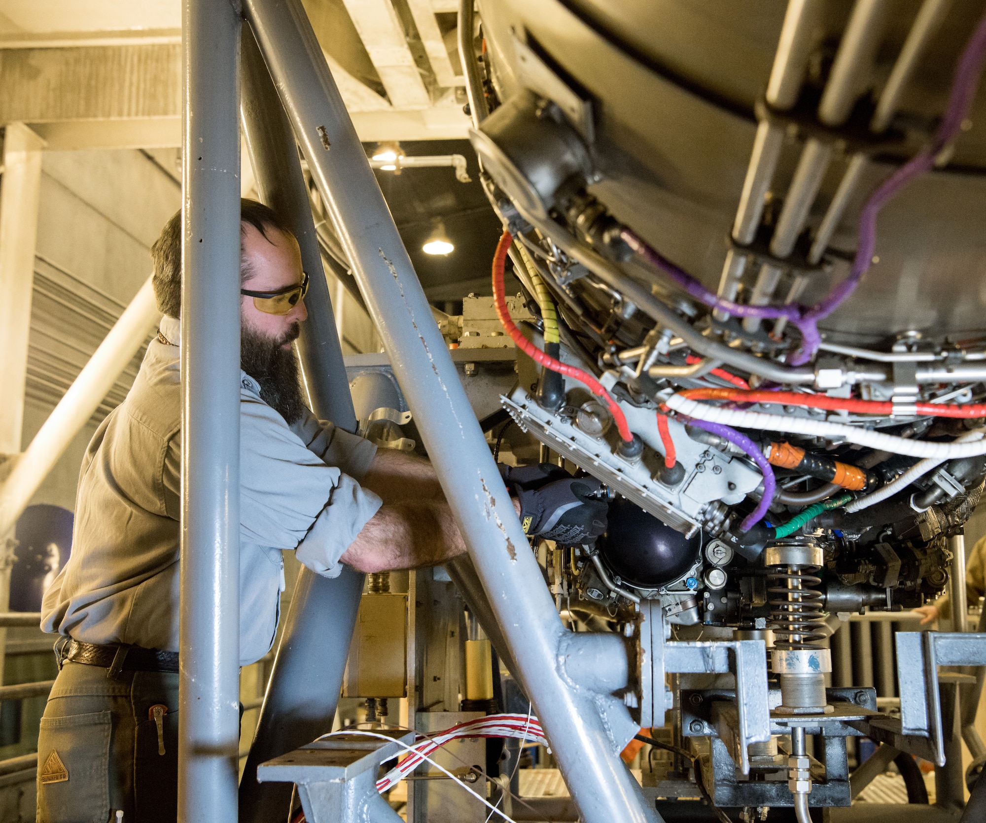 Evan Milligan, a journeyman wireman, connects cables to a F404 engine Jan. 10, 2020, in a sea level test cell at Arnold Air Force Base, Tenn. The engine is being prepared for use as a testbed by the Arnold Engineering Development Complex Technology, Analysis and Evaluation Branch. (U.S. Air Force photo by Jill Pickett)