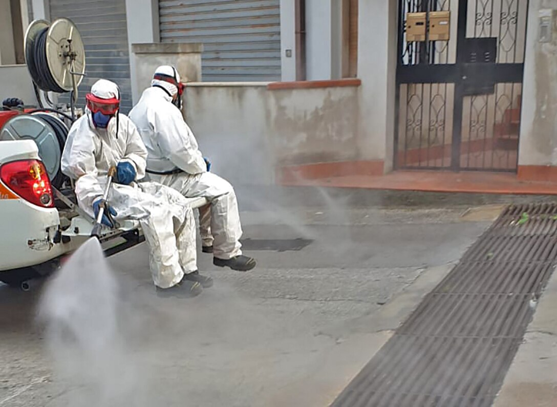 Street cleaners spray while wearing anti-virus suits.