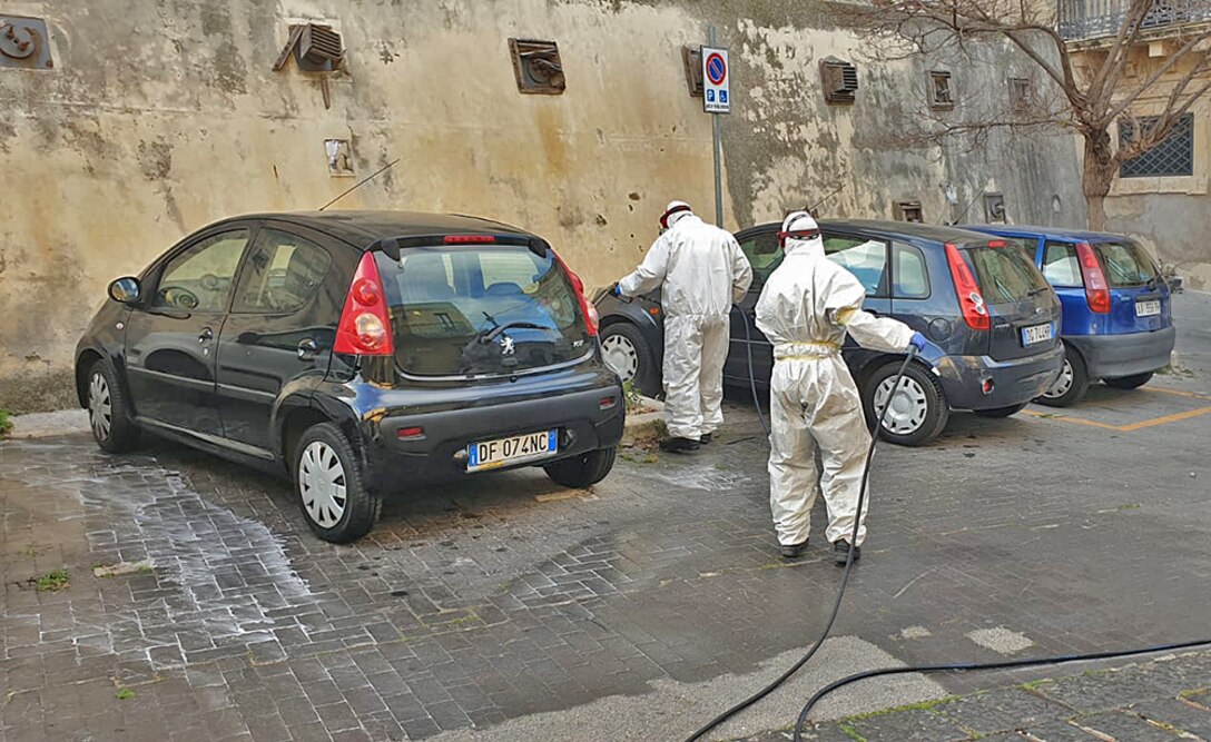 Volunteers in hazmat suits spray down cars in Sicily.