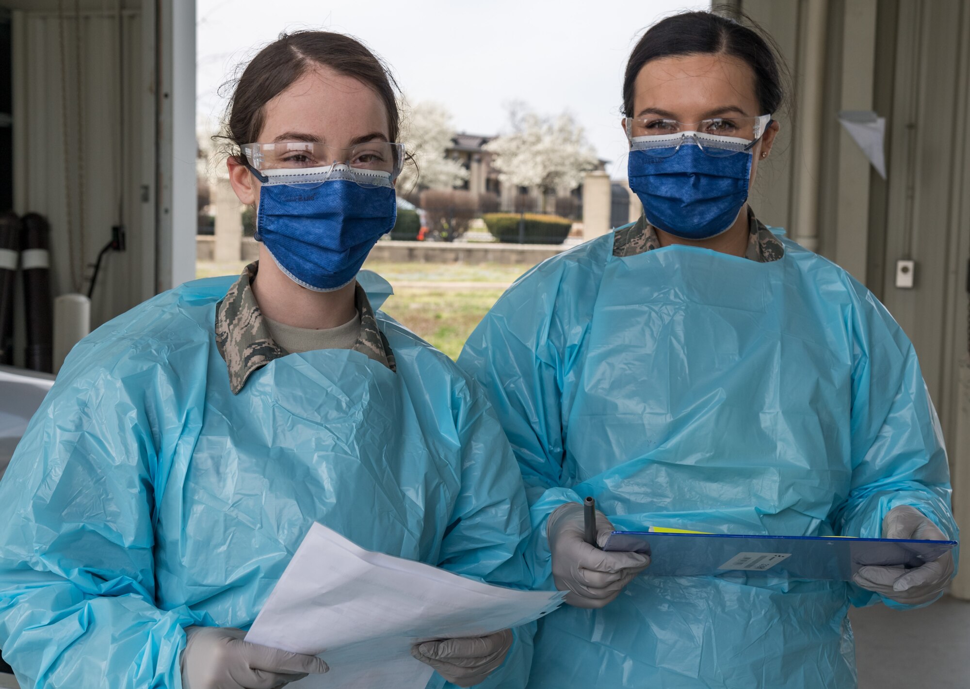 Airman 1st Class Christina Noel, left, and Hope Vusich, right, both assigned to the 436th Operational Medical Readiness Squadron, stand ready to ask base clinic patrons three questions as part of the screening process March 18, 2020, at the main gate on Dover Air Force Base, Delaware. Screening clinic patrons in their vehicle mitigates the possible transmission of COVID-19. (U.S. Air Force photo by Roland Balik)
