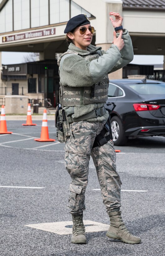 Airman 1st Class Glenda Heredia, 436th Security Forces Squadron response force leader, signals a vehicle driver to display their wristband prior to departing the screening area March 18, 2020, at the main gate on Dover Air Force Base, Delaware. Patrons destined for the base clinic were directed by 436th SFS personnel to a screening area attended by 436th Medical Group personnel prior to allowing them to proceed to the base clinic. Screening clinic patrons in their vehicle mitigates the possible transmission of COVID-19. (U.S. Air Force photo by Roland Balik)