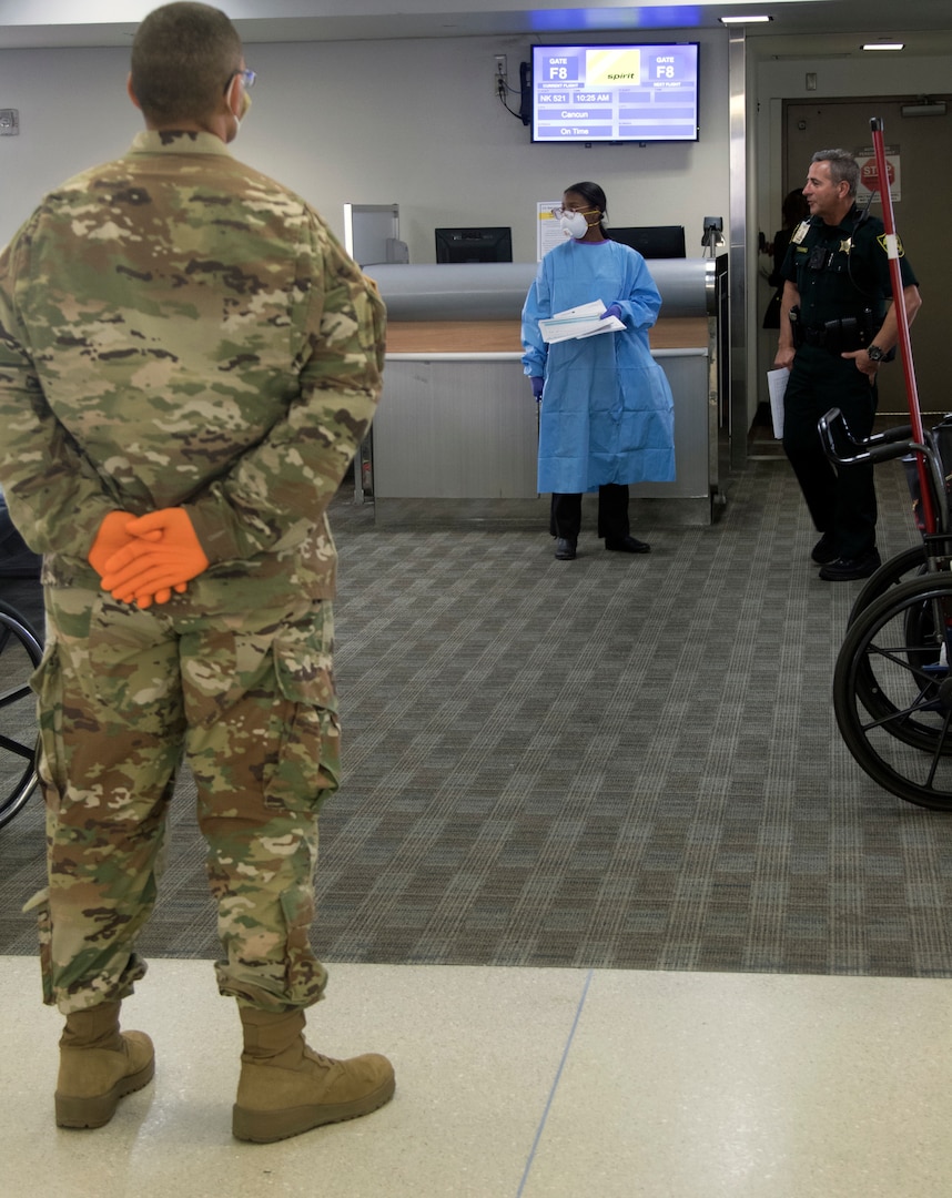 Florida National Guard Spc. Joe Morales-McCullers, 13th Army Band Miramar Fla., waits for passengers arriving from the New York area at Fort Lauderdale-Hollywood International Airport, March 25, 2020. The 13th Army Band is helping screen the passengers to slow the spread of the coronavirus.