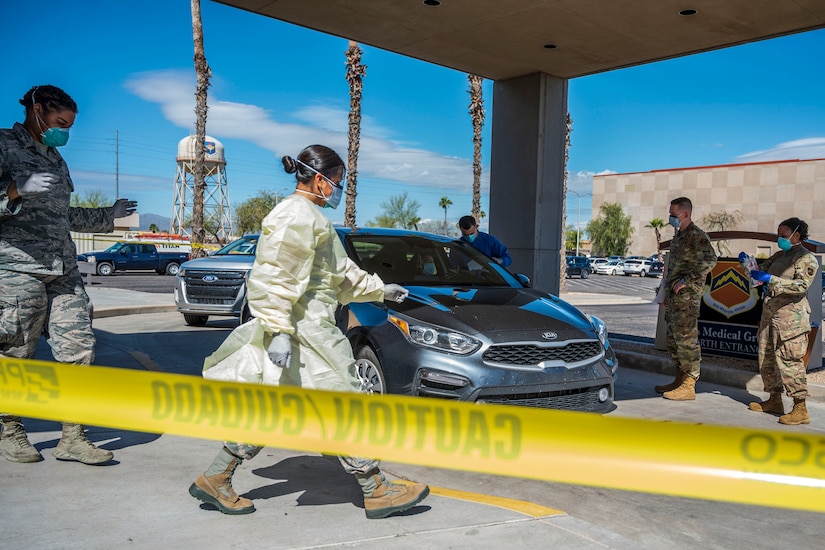 Airmen wearing protective garb gather near a car.