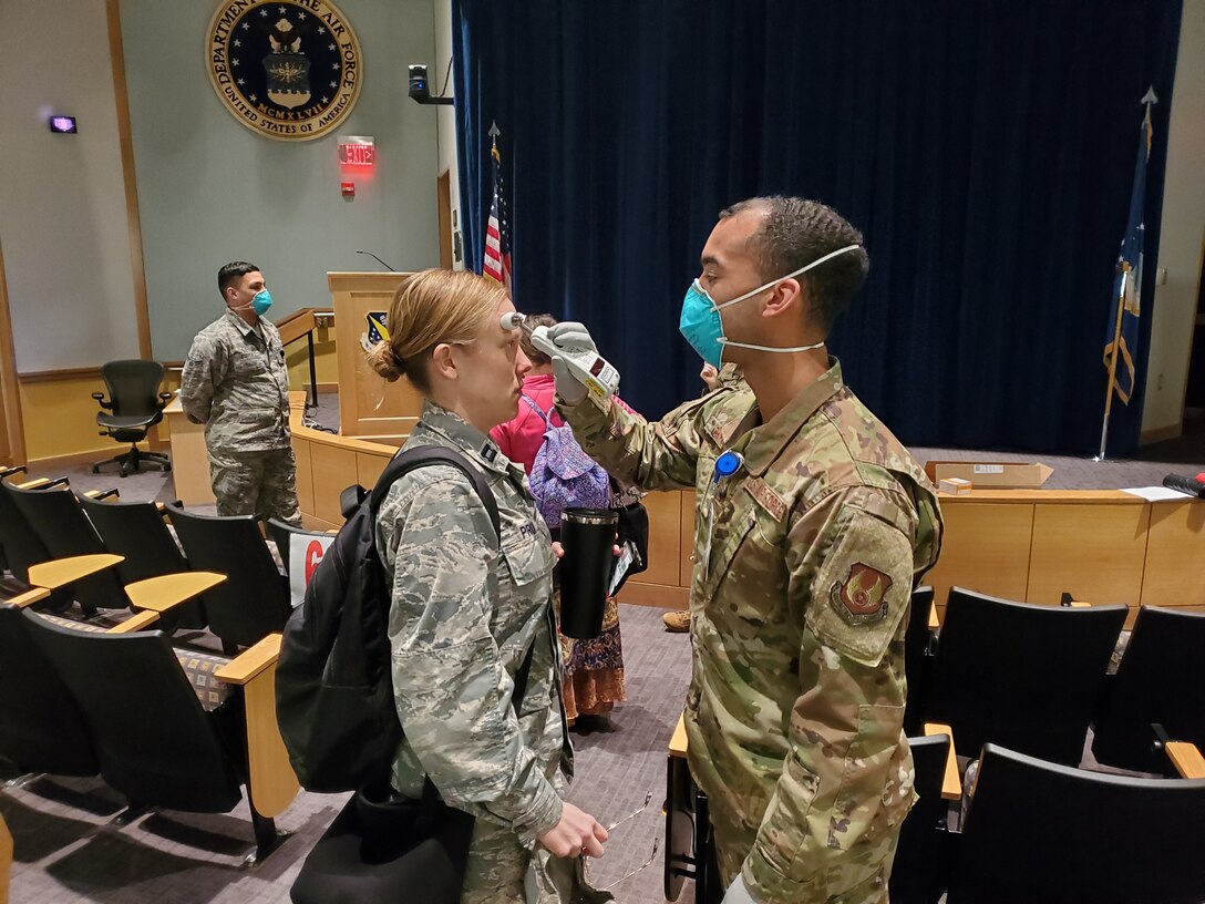 Airman 1st Class Luis Cintron, a dental technician at the Wright-Patterson AFB Medical Center, takes a temperature reading from Capt. Kelsey Pruitt, a nurse practitioner with the Women’s Health Center as she arrives for duty March 25. All medical center staff members are now having their temperatures checked upon arriving for duty at the medical center at one specified location. (U.S. Air Force photo/Bryan Ripple)