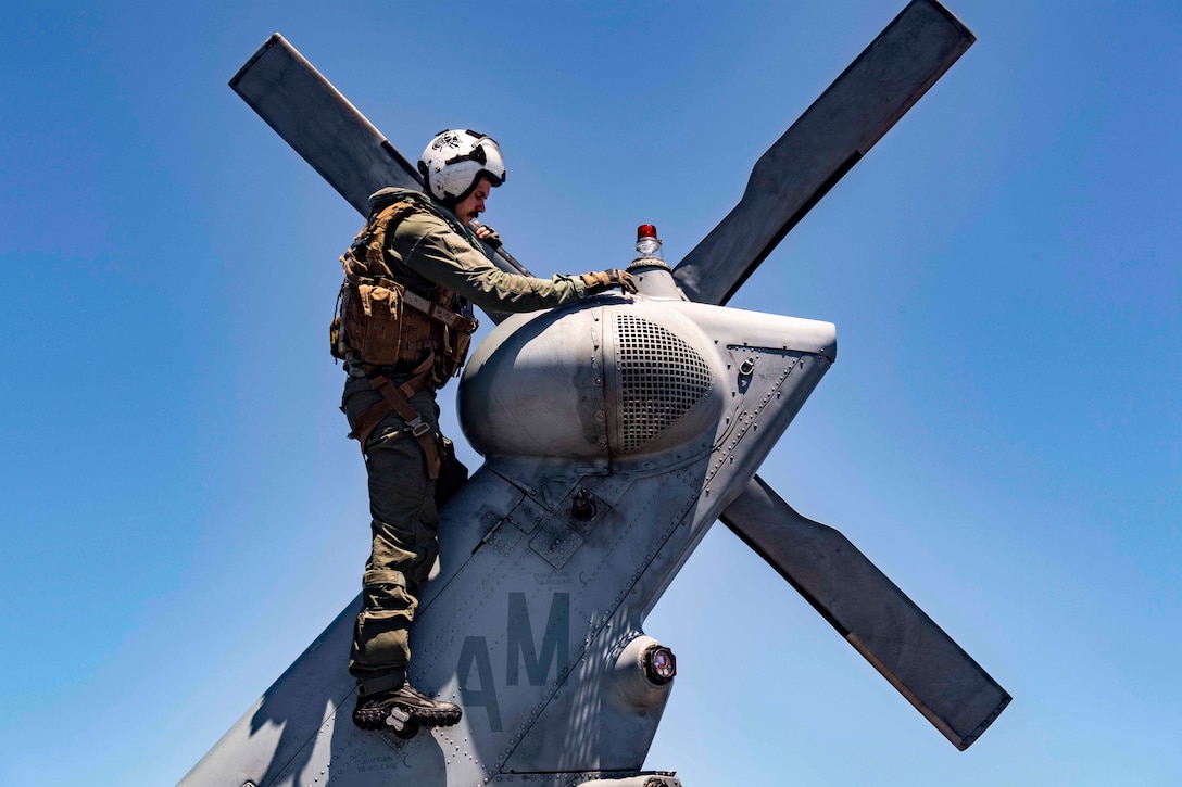 A sailor stands on the tail of a helicopter.