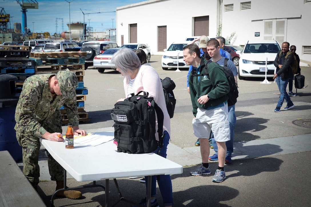 Reservists in civilian clothes line up at a table manned by a sailor in uniform.