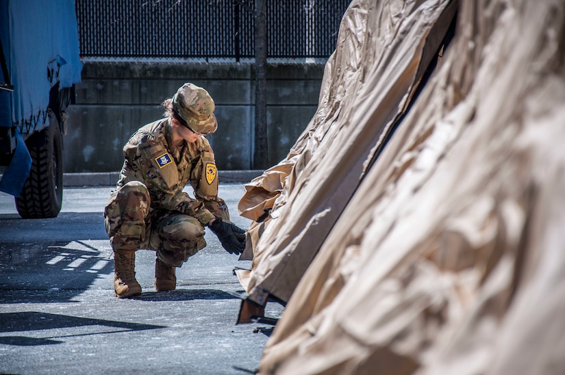 A soldier kneels outside a tent.