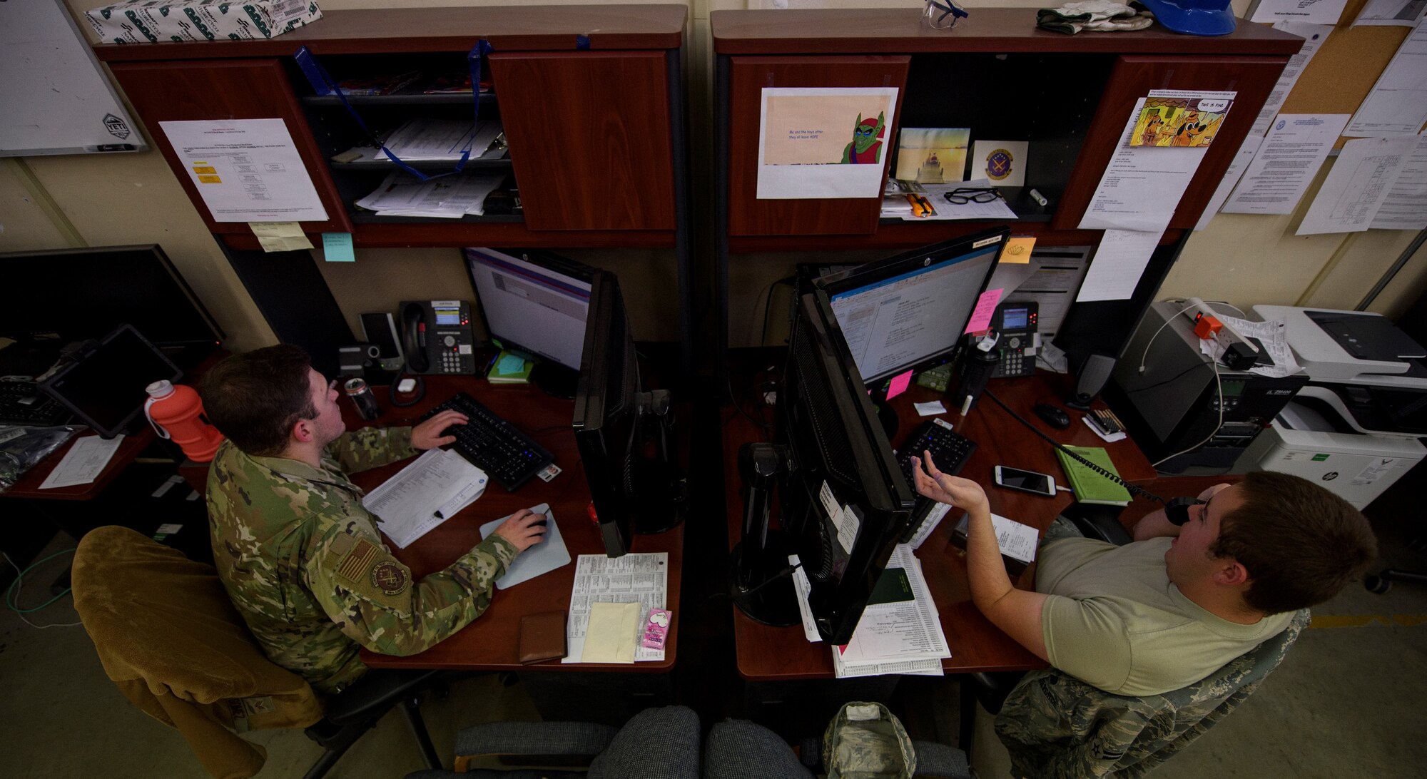 Two Airmen sit at their desk.