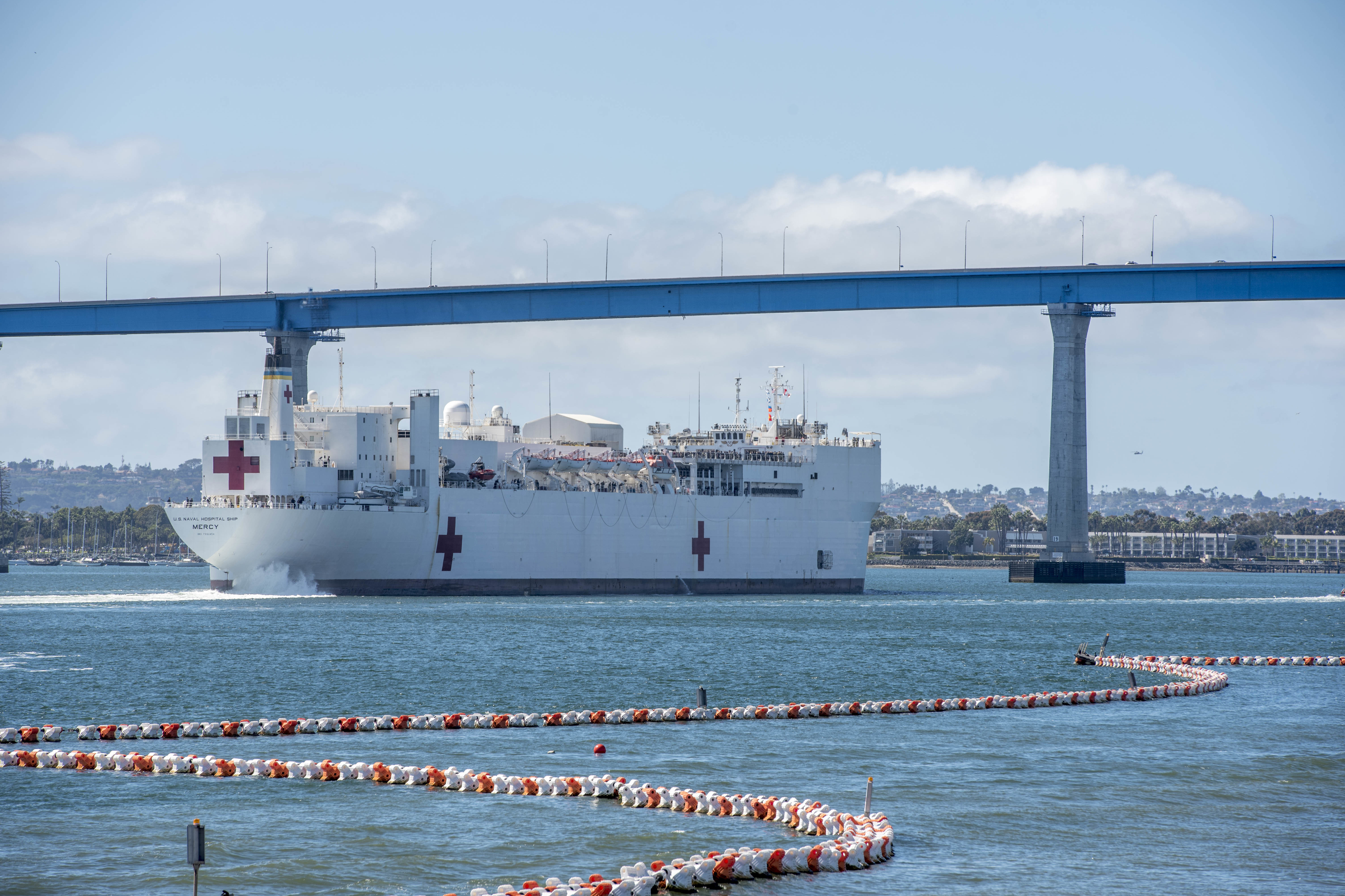 A military hospital ship sails under a bridge as it makes its way out to sea.