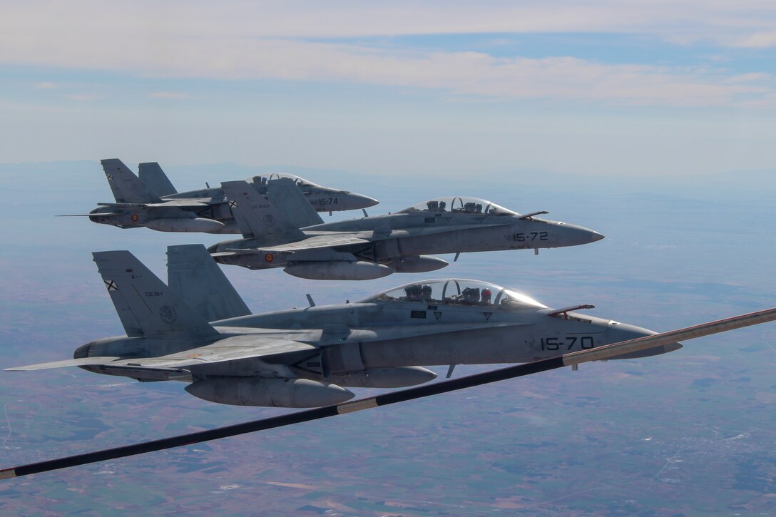 Spanish Air Force F18 Hornets with the 11th Wing fly in formation next to a U.S. Marine Corps KC-130J