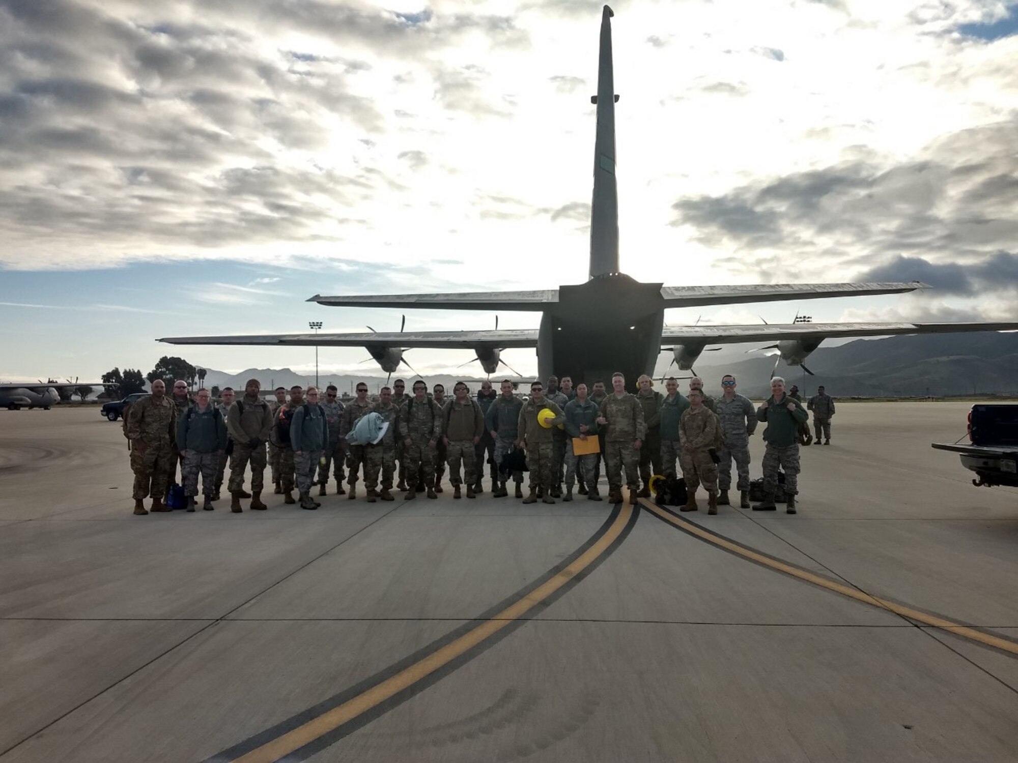 Photo of a large group of airmen traveling to the Riverside County Fairgrounds to assist with assembling medical beds posing for a group photo behind a C-130J aircraft at the Channel Islands Air National Guard Station, Port Hueneme, California.