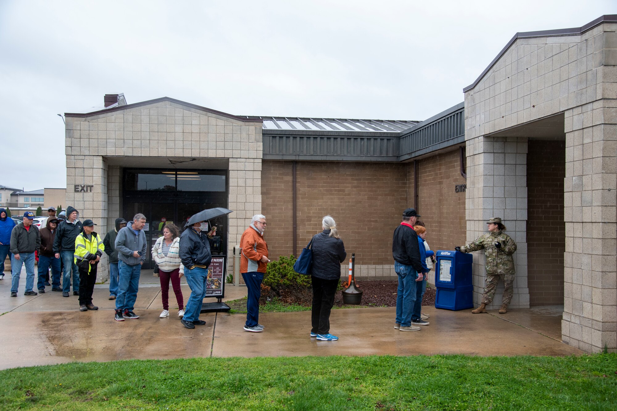 Shoppers form a line outside the Dover Air Force Base , Delaware Commissary on March 25, 2020, while base Chiefs and First Sergeants check IDs and keep a guest count; seventy-five guests were allowed in the building at a time. The Chiefs Group and First Sergeants volunteered at the Commissary checking IDs, assisting with social distancing measures, and stocking shelves to help mitigate the spread of COVID-19, reduce confusion and ensure Airmen and their families still had access to essential items. (U.S. Air Force Photo by Airman 1st Class Jonathan Harding)(U.S. Air Force Photo by Airman 1st Class Jonathan Harding)