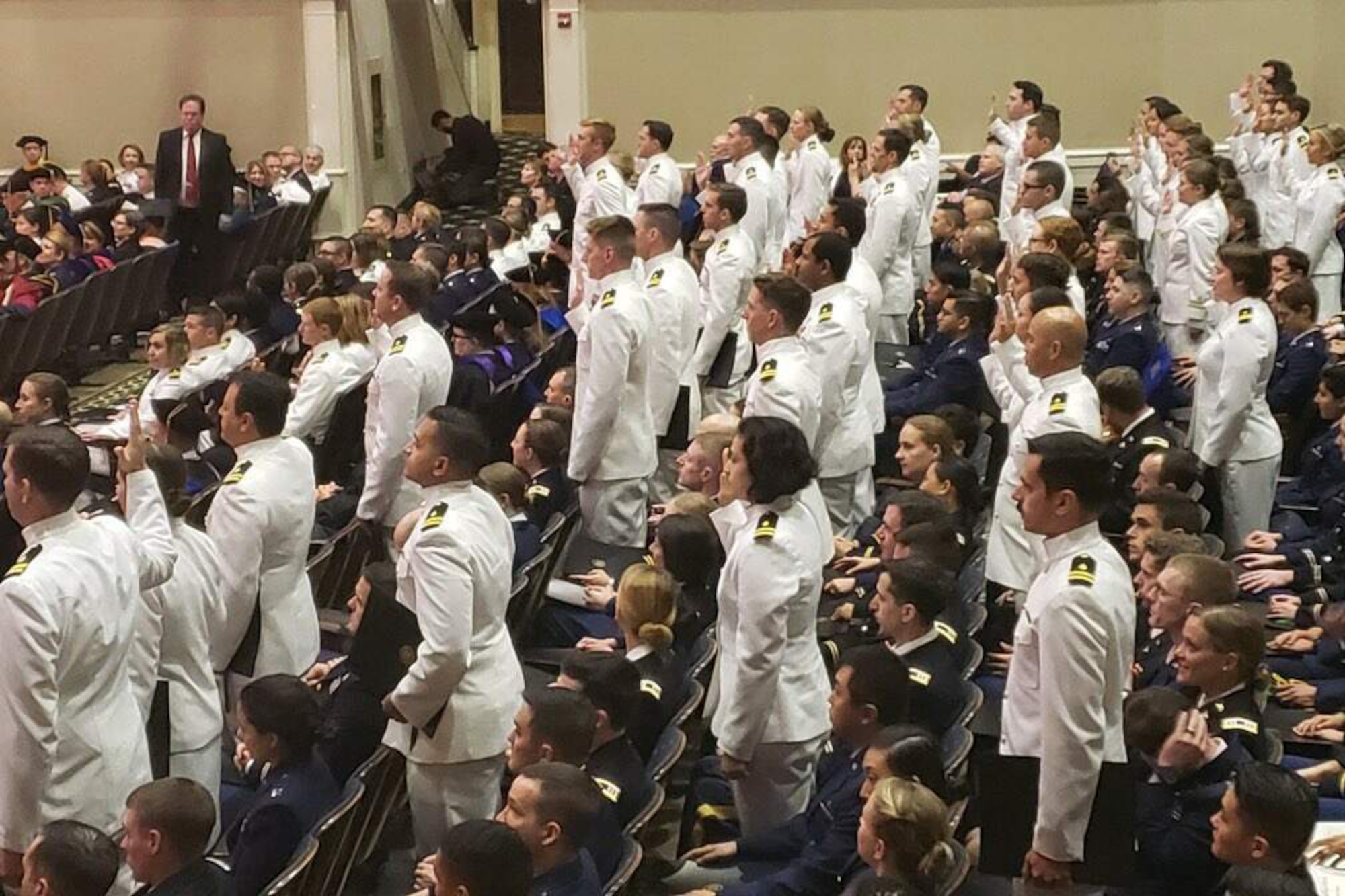 Service members stand at their seats in an auditorium and raise their right hands.
