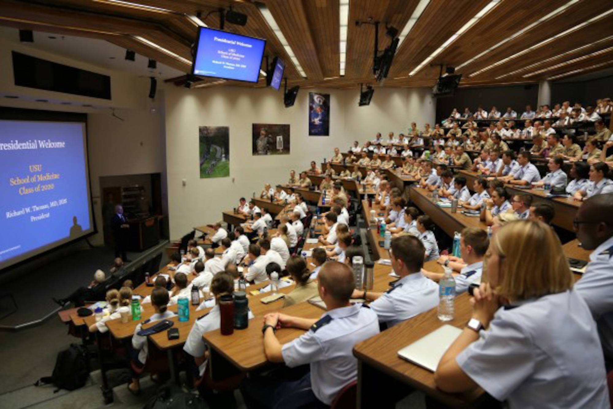 Medical students fill an auditorium lined with wall-mounted screens.