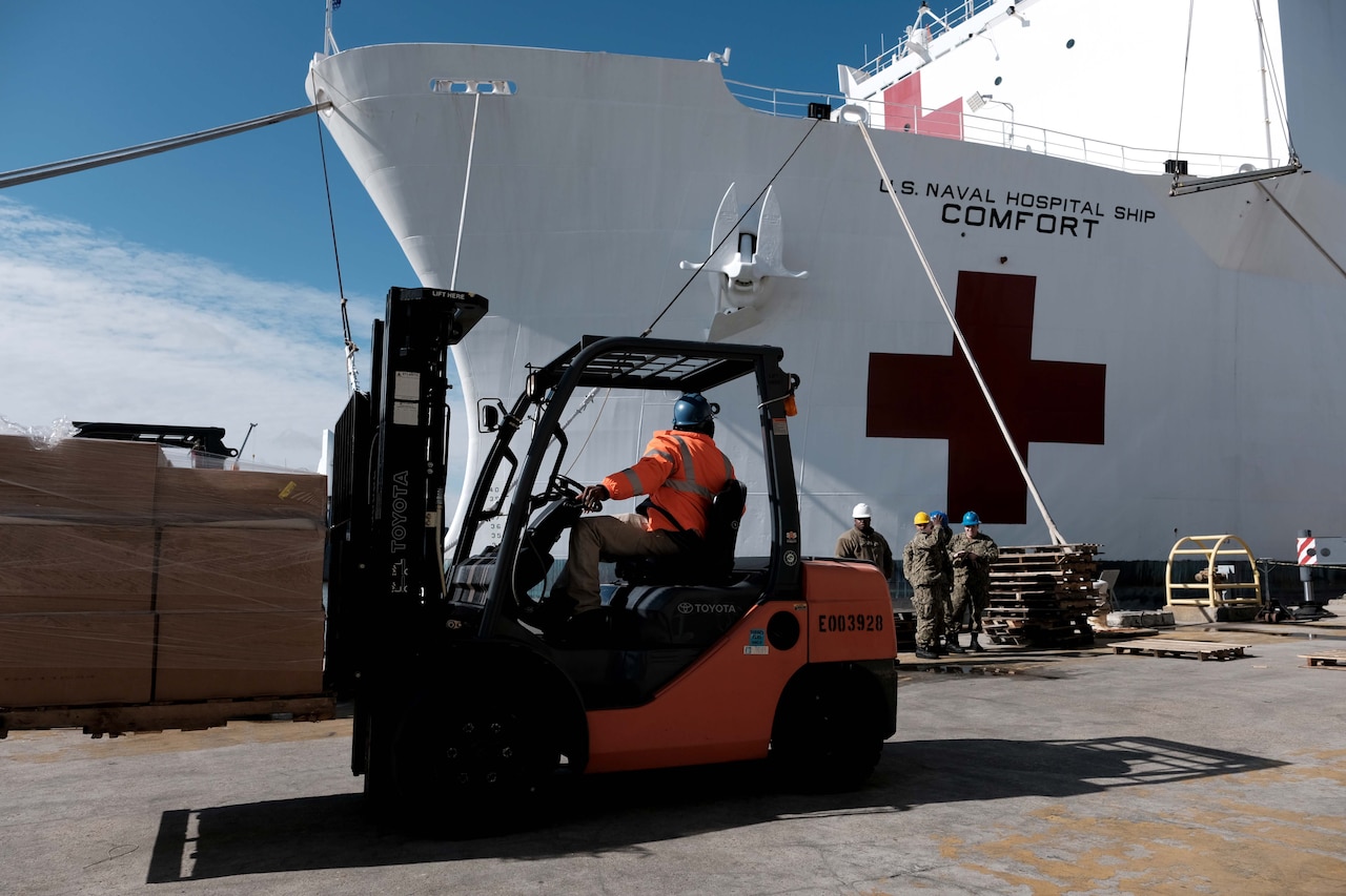 A forklift operator positions his load on dock in front of a ship.