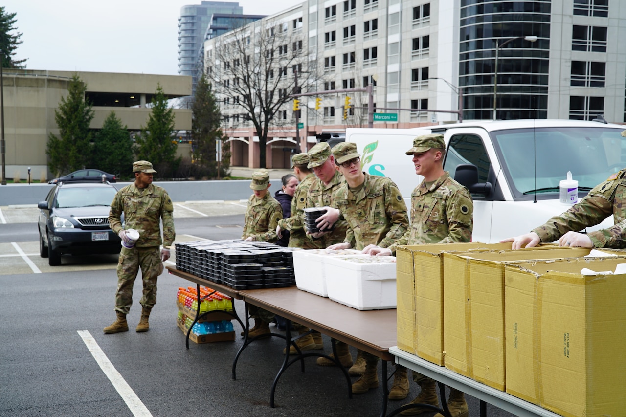 Soldiers move packaged hot meals to a long table.